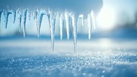 Sparkling icicles hanging against blurred winter background with fresh snow crystals beneath, creating natural cold season atmosphere for seasonal designs.