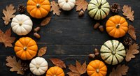 Autumn pumpkins arranged in circle with fall leaves, acorns and pine cones on dark wooden background. Seasonal harvest decoration for thanksgiving and halloween.