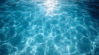 Sunlight creates mesmerizing ripple patterns on crystal clear turquoise water surface, with natural caustic effects and light reflections creating dynamic movement.