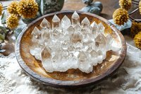 Clear quartz crystal points arranged on rustic wooden plate with dried yellow flowers, creating mystical healing altar display on textured linen fabric background.