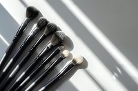 Professional makeup brushes with soft bristles arranged in row on gray surface with dramatic shadow lines, ideal for beauty industry content.