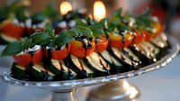 Grilled eggplant slices topped with fresh tomatoes, mozzarella and basil leaves arranged on silver platter, elegant appetizer presentation with bokeh background.