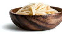 Fresh udon noodles served in rustic wooden bowl against white background, traditional Asian cuisine preparation showing thick wheat pasta strands.