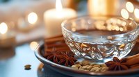 Warm spiced tea in crystal glass bowl with star anise and cinnamon sticks creating cozy autumn atmosphere with golden bokeh lights background.