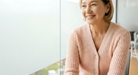 Middle-aged Asian woman wearing pink cardigan smiling indoors, suitable for lifestyle, wellness, and corporate business content.