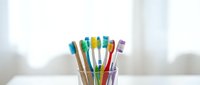Colorful bamboo toothbrushes with rainbow bristles in glass holder on white bathroom counter for eco-friendly oral hygiene and sustainable dental care routine.