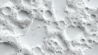 White soap foam with bubbles and suds creating abstract texture pattern on light background, macro photography showing detailed surface structure of cleaning product.