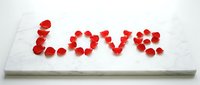Red rose petals arranged to spell Love on a white marble surface, romantic Valentine's Day concept for cards, decor, and celebrations.