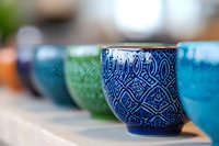Colorful ceramic tea cups with ornate traditional patterns lined up in blue, green and turquoise tones, shallow depth of field creates artistic composition.