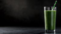 Fresh green smoothie in tall glass with straw on dark background for healthy lifestyle and nutrition concepts.