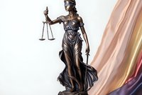 Bronze statue of Lady Justice holding scales and sword against soft pink background, symbol of law and justice system, isolated on light backdrop.