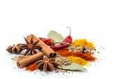 Aromatic cooking spices and herbs scattered on white background including cinnamon sticks, star anise, bay leaves, chili peppers and colorful ground seasonings.