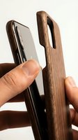 Smartphone in wooden case held by hand showing protective wood phone cover design for mobile device protection and accessory display.