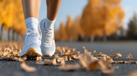 Female feet in white sneakers jumping on fallen autumn leaves against golden trees background, active lifestyle and seasonal outdoor fitness concept.