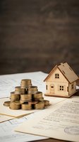 Stacked coins beside a wooden house model on property documents, symbolizing real estate investment, mortgage planning, and home purchase finance.