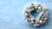 Elegant winter wreath with white pine branches, pastel pink flowers, and silver ornaments on light blue wooden background.