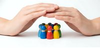 Protective hands covering colorful wooden peg people figures representing family safety, insurance coverage, community support and care concept.