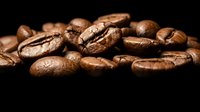 Roasted coffee beans scattered on dark background showcasing rich brown textures and natural cracks for cafe branding and beverage marketing materials.