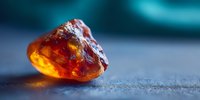 Raw amber stone with golden honey color and natural inclusions on textured surface. Organic gemstone for jewelry making and decorative crafts.