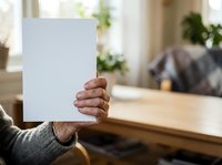 Person holding blank white paper sheet in front of face indoors, mockup for advertising, marketing campaigns, or promotional messaging in home environment.