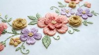 Delicate hand embroidered floral design with colorful thread flowers on white fabric showcasing traditional needlework craftsmanship and textile art.