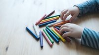 Child hands selecting colorful crayons on wooden table for creative art project. Educational activity promoting imagination and artistic development.