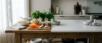 Modern kitchen interior with wooden island, fresh herbs, and colorful vegetables on marble countertop for healthy cooking and meal preparation.