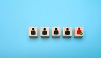 Wooden blocks with person icons in a row, one highlighted in red with a green checkmark, symbolizing selection or recruitment on blue background.
