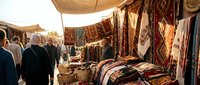 Traditional carpet and textile market with colorful handwoven rugs displayed under canvas awnings while customers browse authentic Middle Eastern crafts.