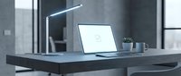 Modern minimalist workspace with laptop computer and desk lamp on dark wooden table in contemporary office interior with natural lighting.