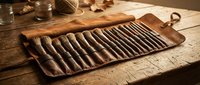 Professional leather tool roll with metal instruments organized in slots on rustic wooden workbench for craftsman workshop and artisan projects.