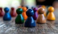 Colorful wooden game pieces on rustic table with focus on blue pawn, symbolizing leadership, diversity, and teamwork concepts in business settings.