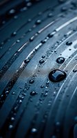 Water drops on dark metallic surface with curved lines creating dramatic contrast and reflection, macro photography showing intricate details and texture.