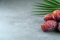 Fresh Medjool dates with palm leaves on gray stone surface for healthy snacking and Middle Eastern cuisine preparation.