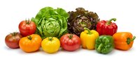 Fresh organic vegetables including colorful bell peppers, ripe tomatoes, green and purple lettuce heads arranged on white background for healthy cooking.