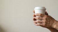 Close-up of mature male hand holding blank white container with lid against neutral background, suitable for product mockups, healthcare, supplements, or cosmetics branding.