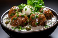 Juicy meatballs in creamy mushroom sauce garnished with fresh parsley and capers, served in dark ceramic bowl on black background. Food photography.