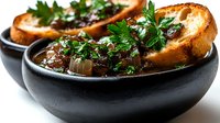 Rich beef stew with tender meat and vegetables served in black bowls with crusty bread slices, garnished with fresh parsley for comfort food dining.