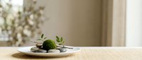 Minimalist moss ball arrangement on ceramic plate with stones and dried botanicals on wooden table, soft natural light, zen home decor.