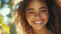 Young African American woman with natural curly hair smiling outdoors in warm sunlight with bokeh background, expressing joy and confidence in casual lifestyle portrait.
