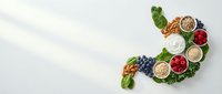 Healthy foods arranged in stomach shape with fresh vegetables, fruits, nuts and grains on white background promoting digestive wellness and nutrition.