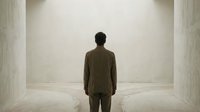 Businessman standing alone in modern minimalist corridor facing bright light, corporate solitude and decision making concept for business presentations.