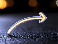 Glowing curved arrow shape emerging from dark textured surface with bokeh lights in background creates magical minimalist composition for business concepts.