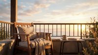 Cozy armchair with blanket on balcony overlooking serene water at golden hour sunset, perfect for relaxation and outdoor living spaces.