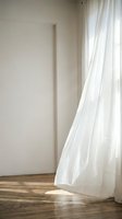 Minimalist interior with sheer white curtains flowing across wooden floor beside blank wall, allowing natural light to create soft shadows and peaceful ambiance for home decor and design projects.