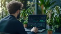 Young Caucasian businessman analyzing financial data and stock market charts on laptop screen while working in green eco-friendly office environment.