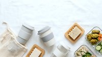Flat lay composition featuring reusable containers, eco-friendly mesh bag, and fresh prepared meals on white background for sustainable lifestyle and meal prep content.