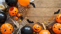 Halloween decorations with orange pumpkins, black balloons, skeleton hands and bat cutouts arranged on rustic wooden background for spooky party setup.