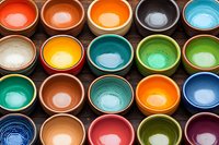Colorful ceramic bowls arranged in rows on dark wooden surface, showcasing vibrant glazed interiors in various colors from orange and blue to green and purple.