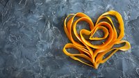 Orange heart shape made from curled butternut squash ribbons on dark textured concrete background, creative healthy food concept for Valentine's day menu.